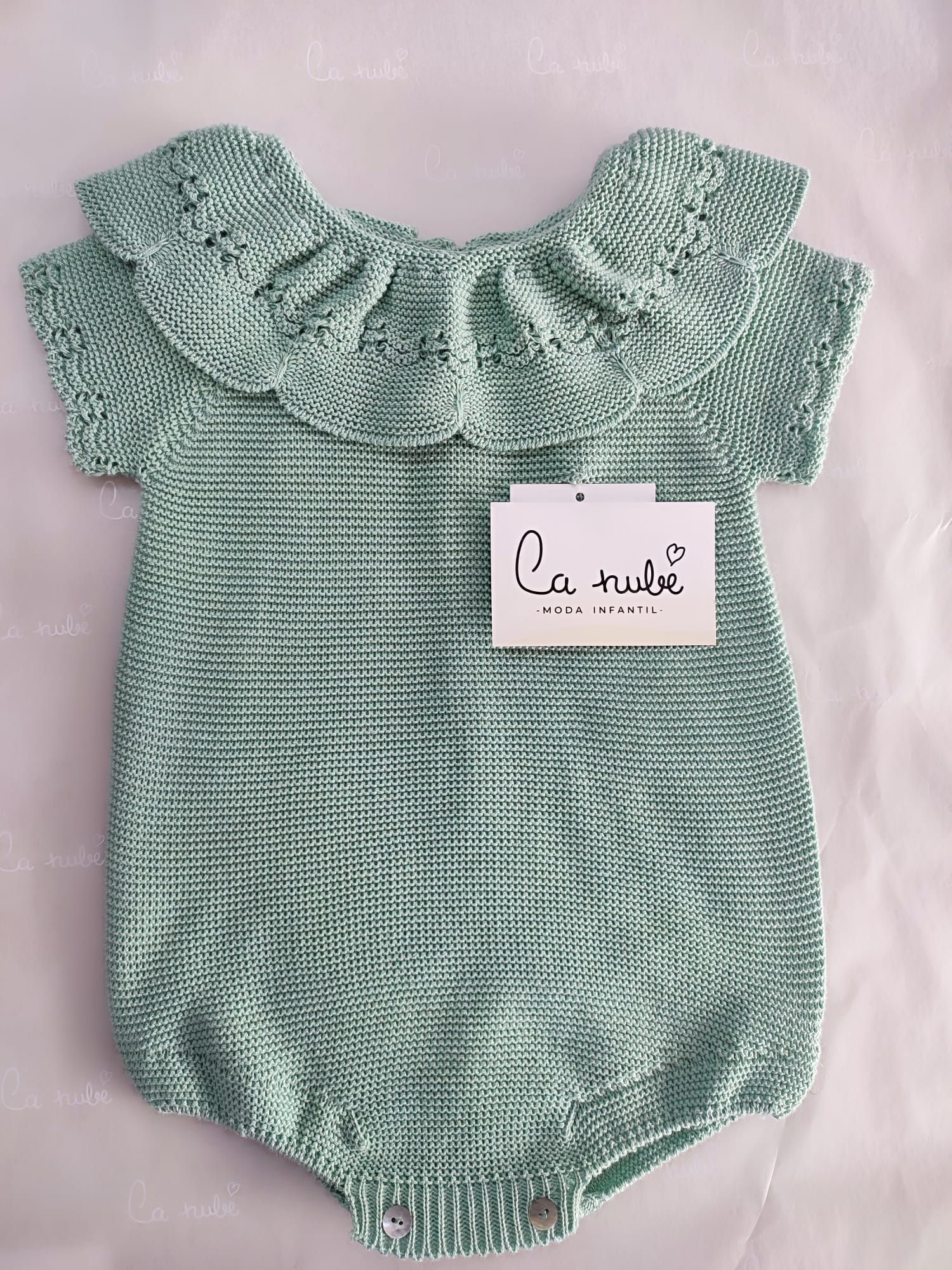 Un bebé lleva un mono de punto verde con cuello con volantes.