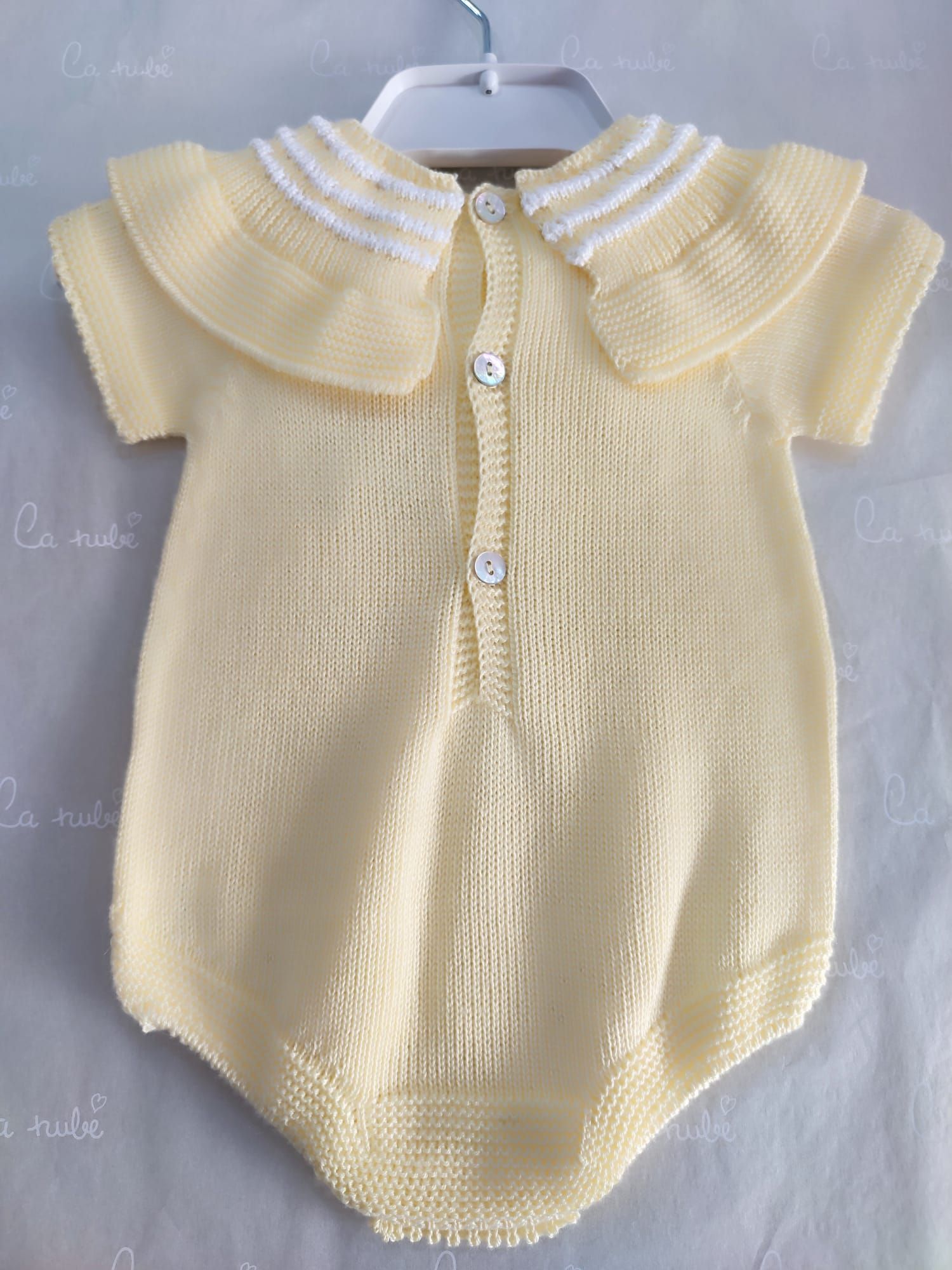 Un mono de bebé de punto amarillo con cuello blanco está colgado en una percha.