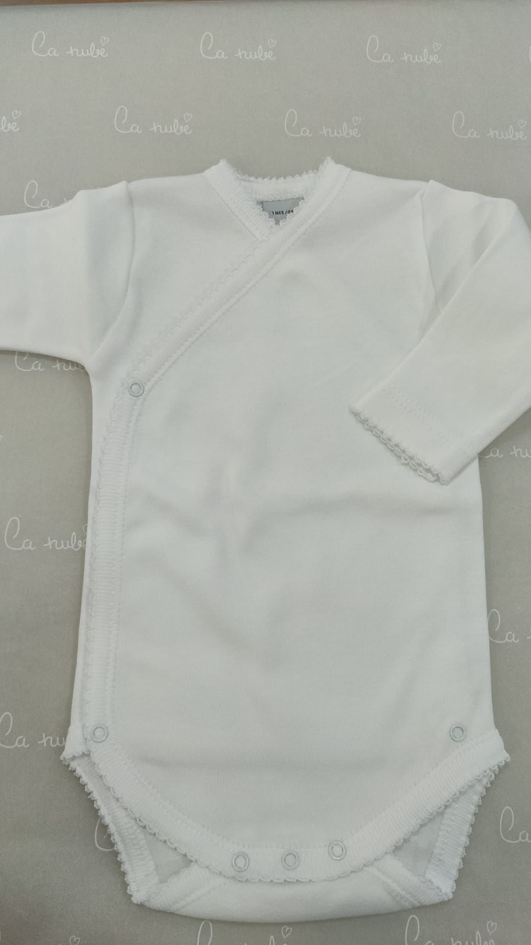 Un mono de bebé blanco con mangas largas está sentado sobre una mesa.