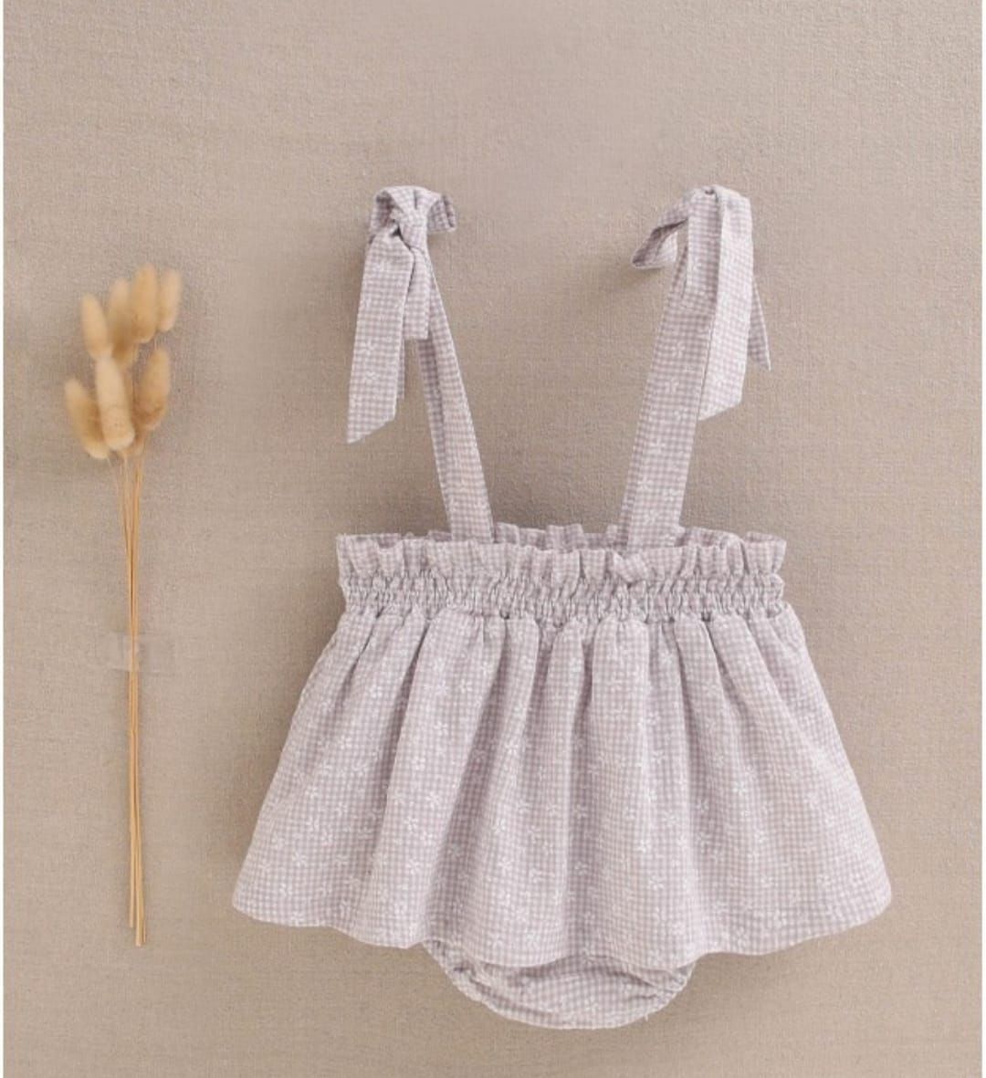 Una niña lleva un vestido gris con una flor en el fondo.