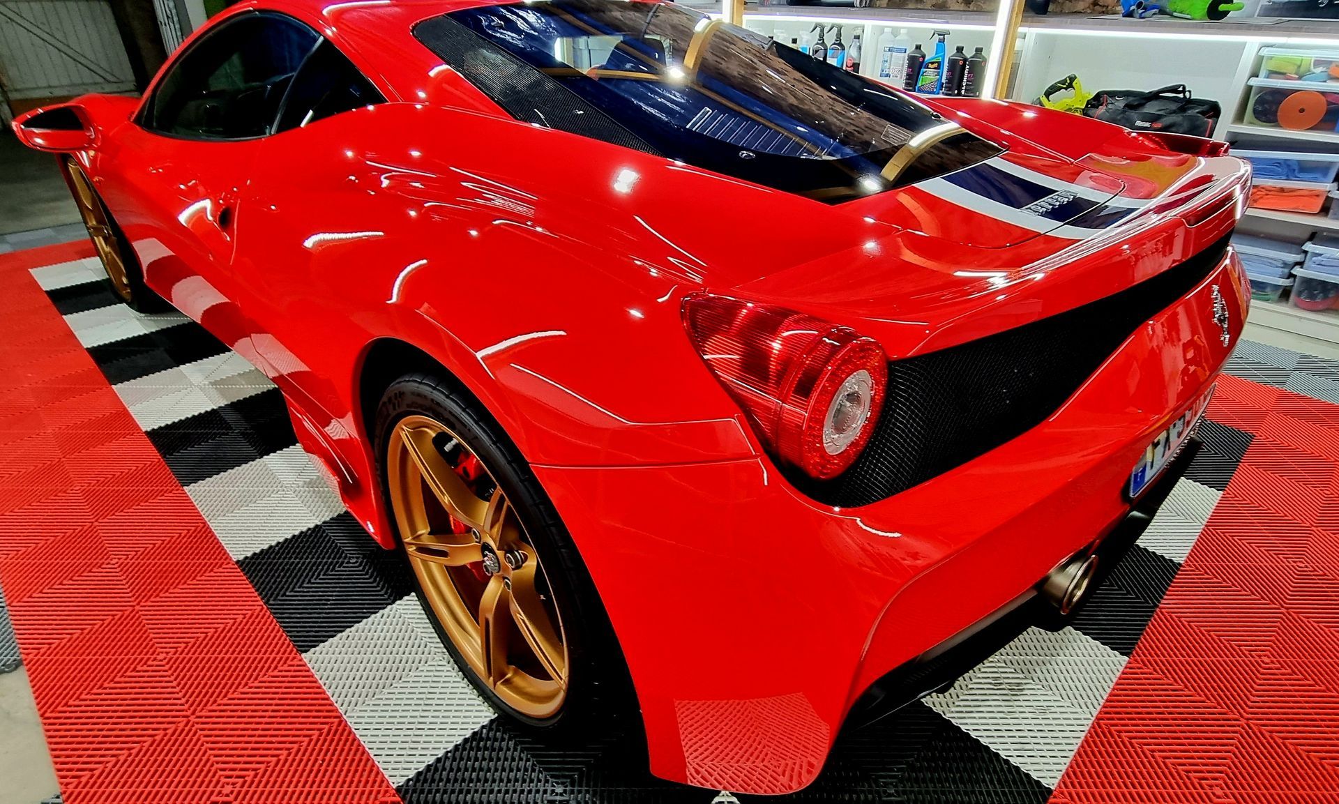 Voiture de sport Ferrari rouge avec des roues dorées garée sur un sol à damier.