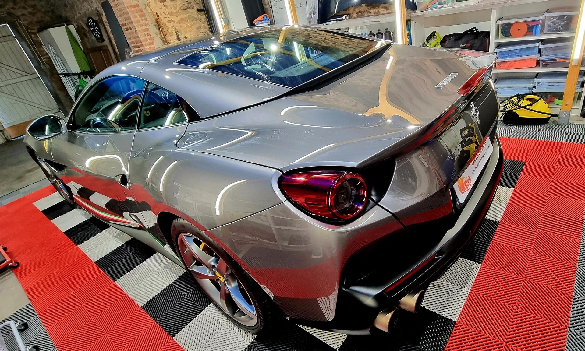 Voiture de sport Ferrari argentée sur un sol à carreaux rouges et noirs.