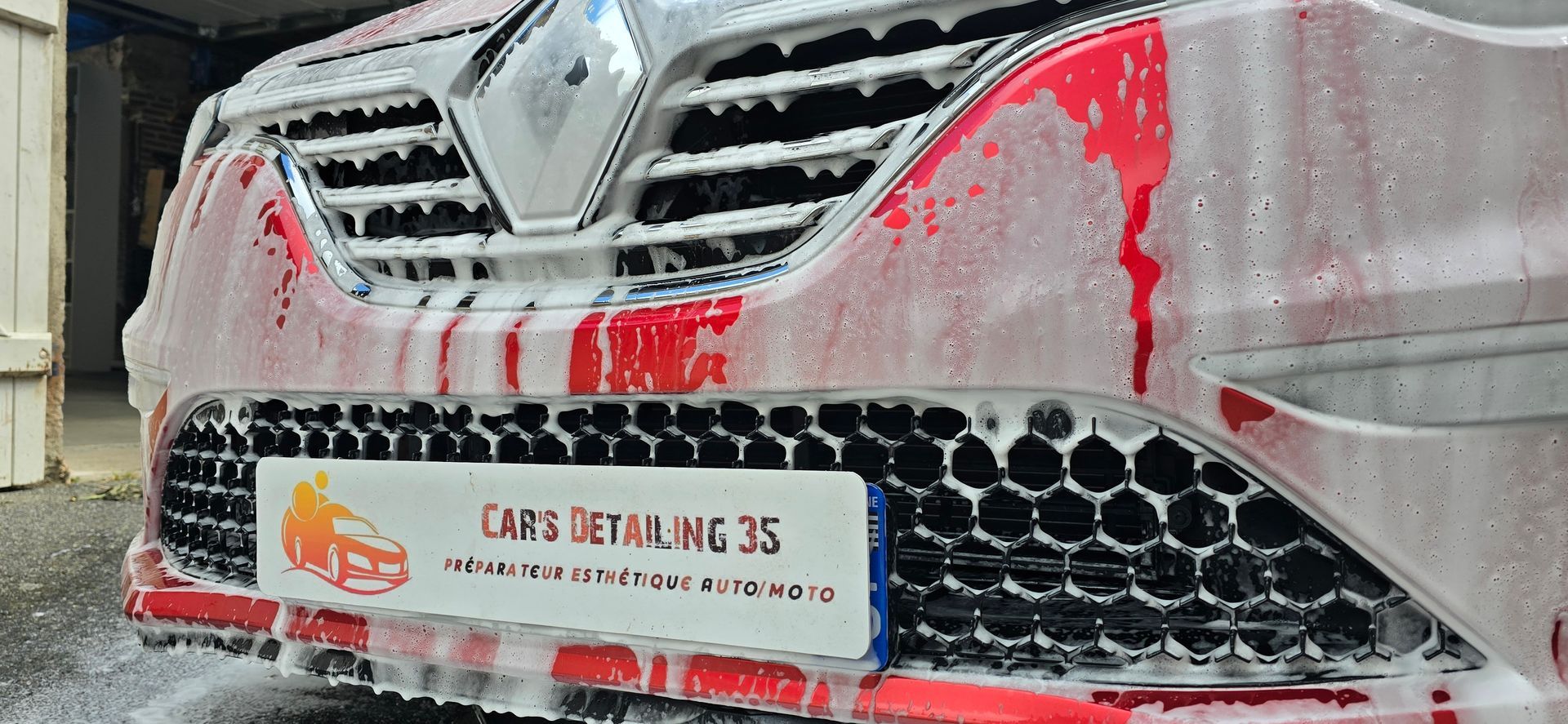 Voiture rouge lavée à la mousse, avec une plaque d'immatriculation indiquant « Cars Detailing 35 ».