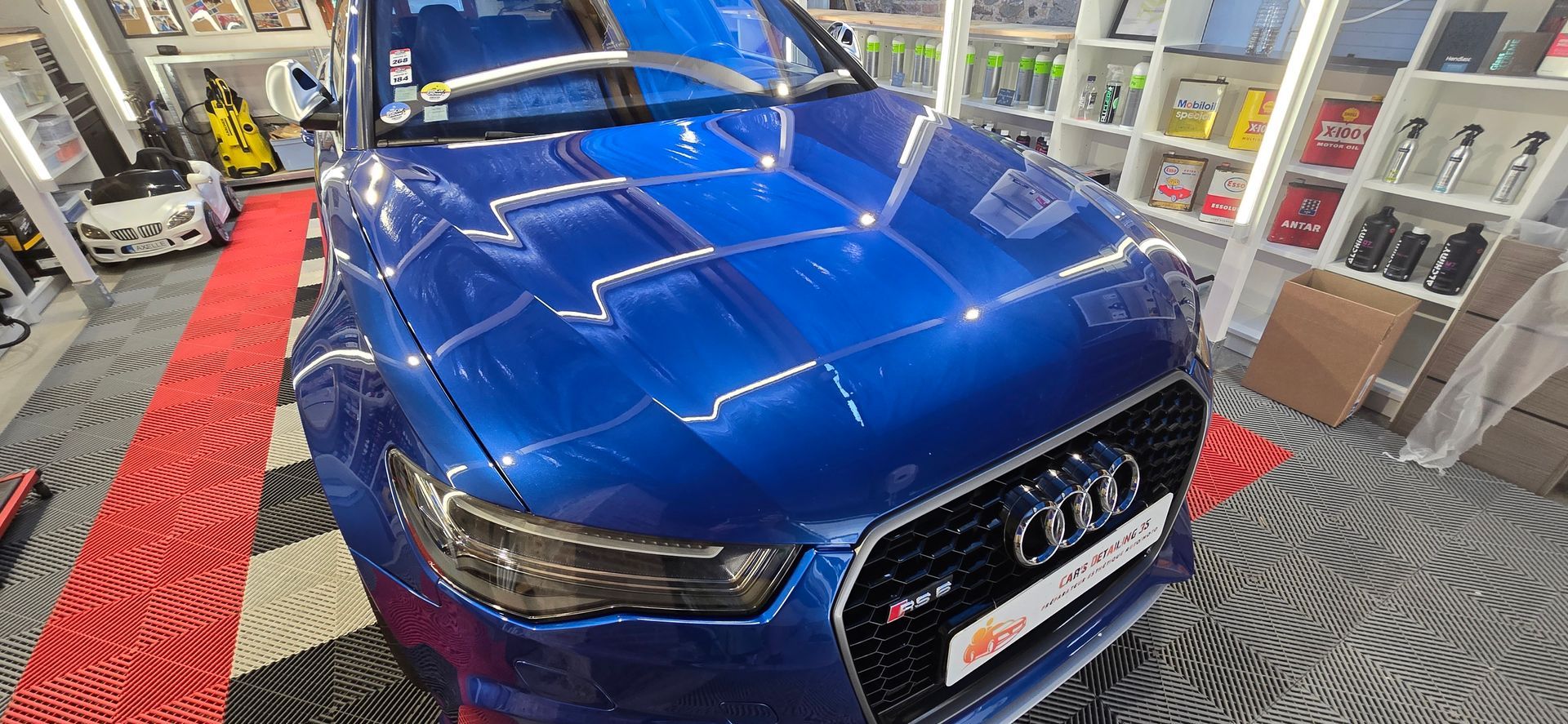 Audi RS6 bleue dans un atelier bien éclairé, reflétant les lumières du plafond.