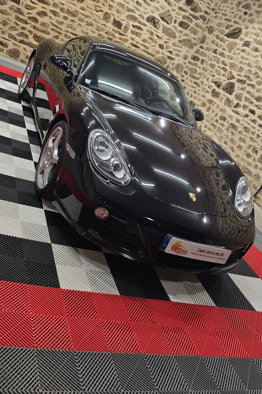 Porsche Cayman noire garée sur un sol en damier.