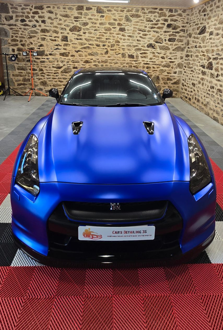 Nissan GT-R bleue avec des accents noirs garée devant un mur de pierre, à l'intérieur d'un garage.