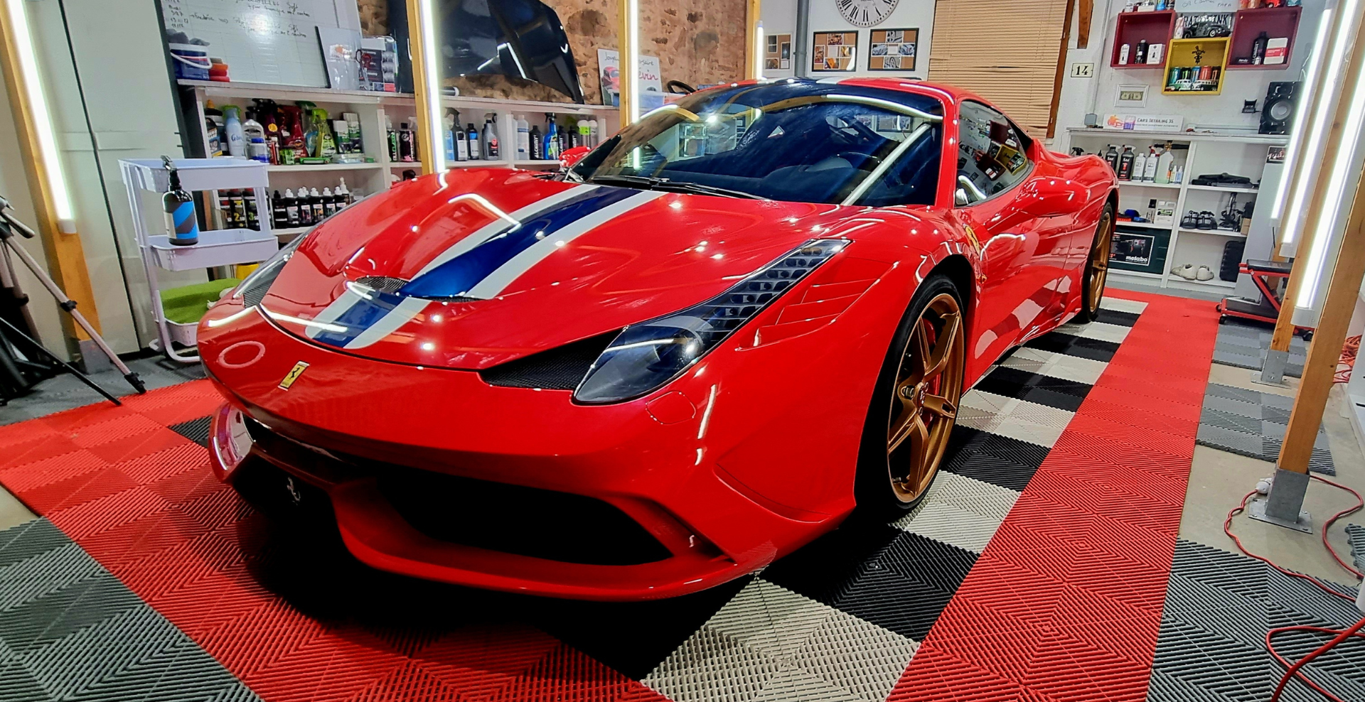 Voiture de sport Ferrari rouge avec bande bleue et blanche, sur sol à damier.