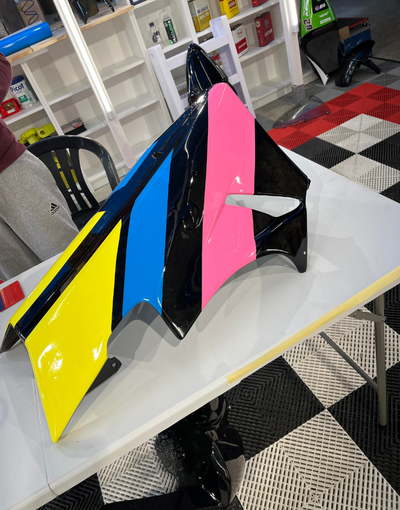 Carénage de moto au design géométrique coloré : jaune, bleu, rose et noir sur fond blanc.