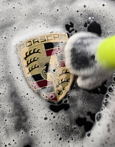 Nettoyage mousseux d'un emblème Porsche doré avec une brosse ; mousse blanche et noire.