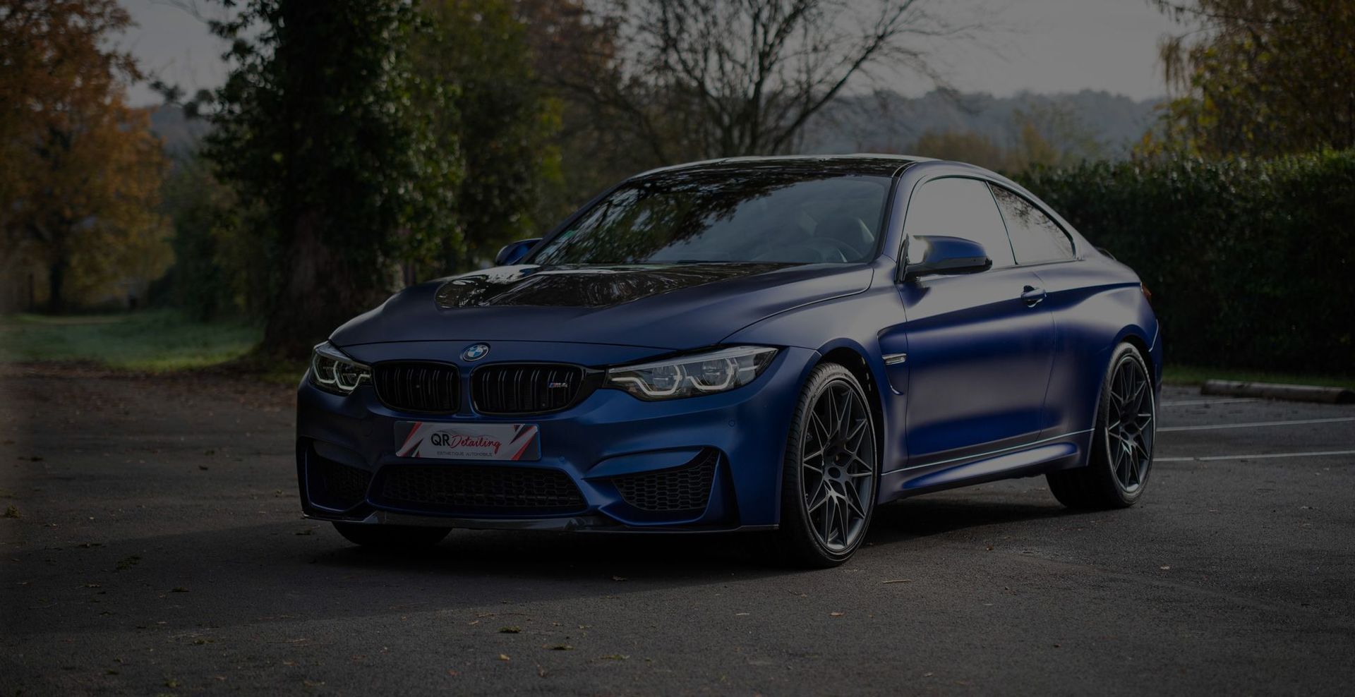 Coupé BMW M4 bleu garé sur asphalte, roues gris foncé, à l'extérieur.