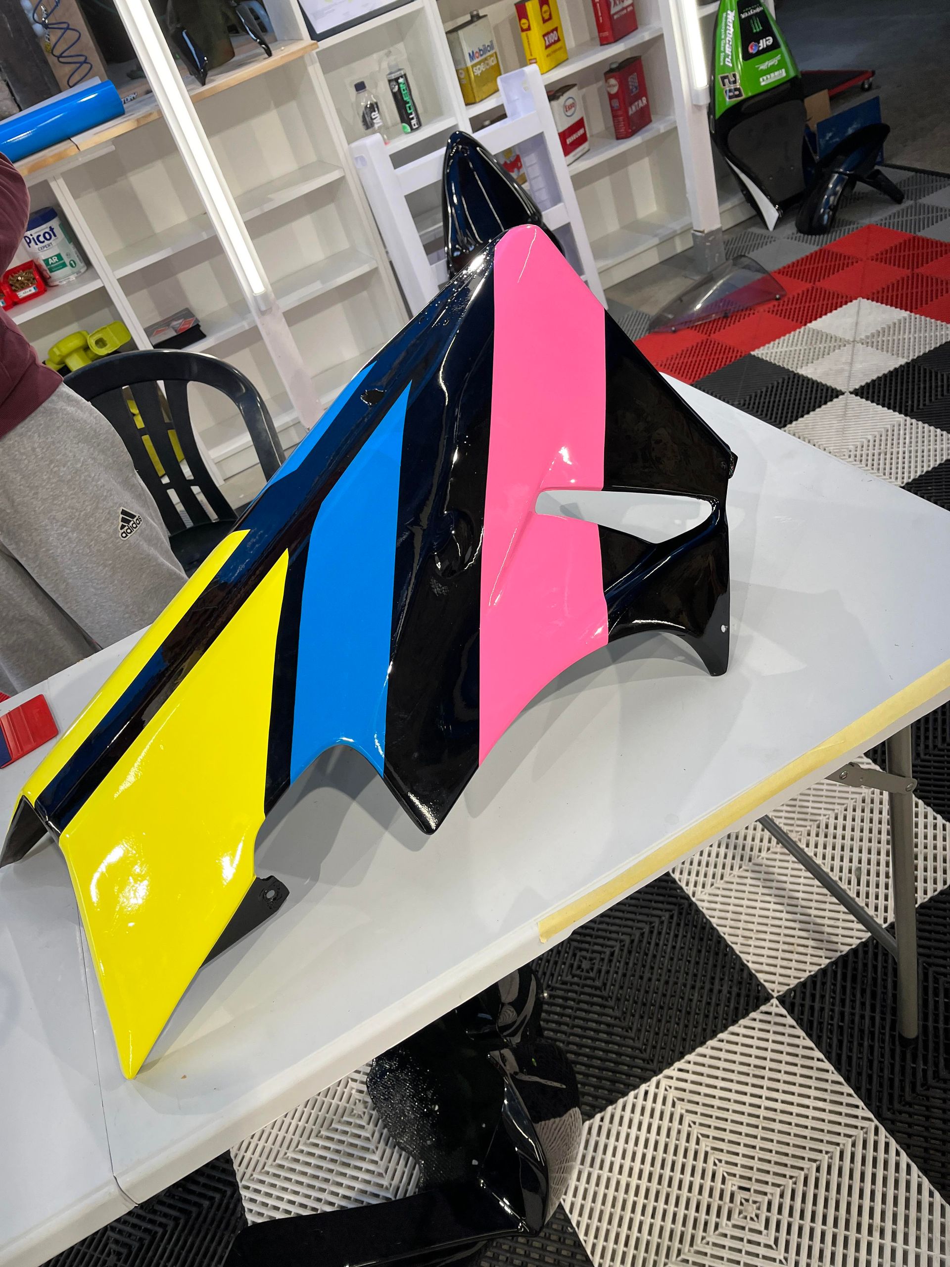 Pièce de voiture colorée en jaune, bleu, rose et noir sur une table, à l'intérieur.