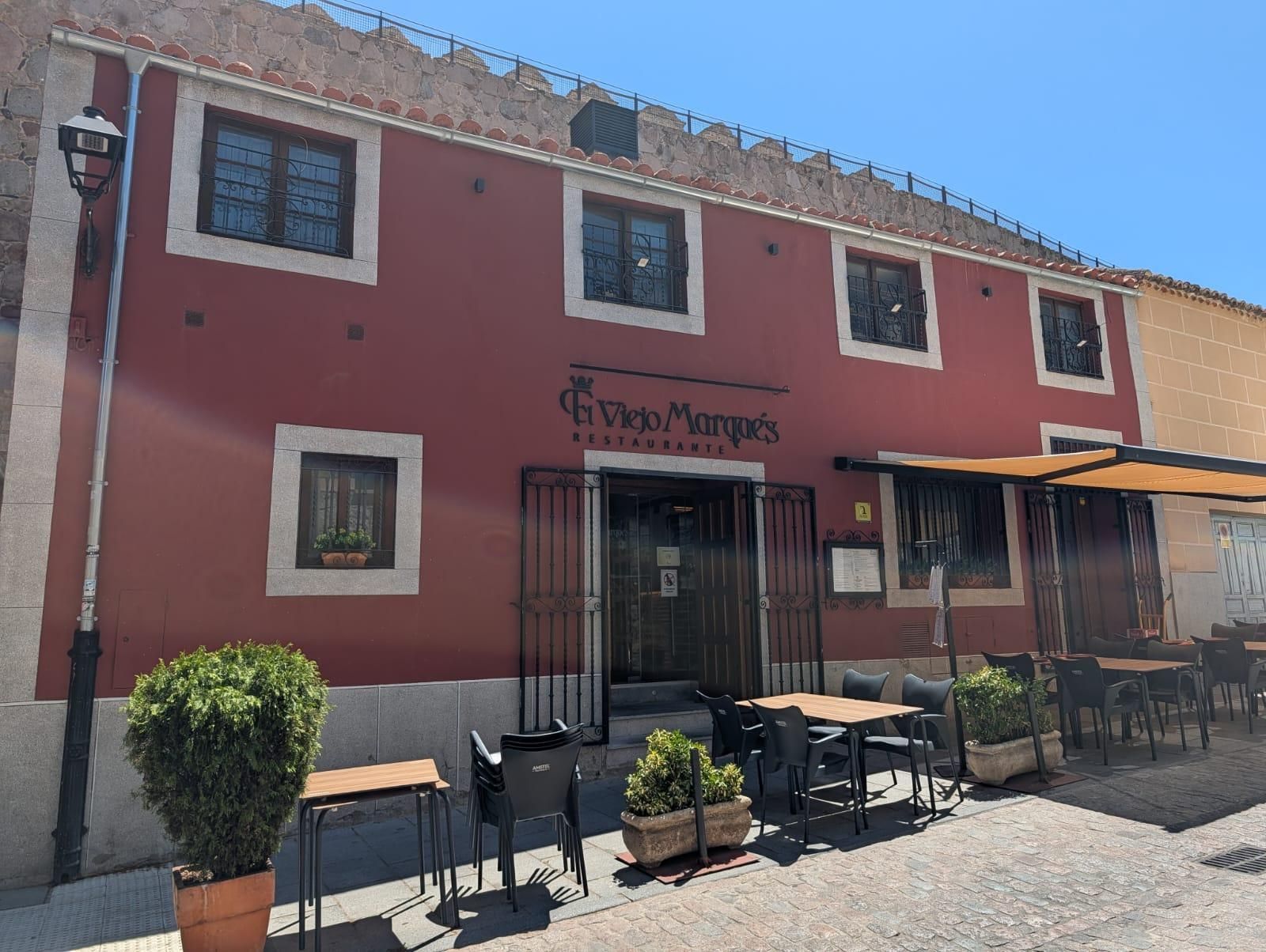Fachada de estuco rosa con mesas y sillas de café al aire libre, bañada por la luz del sol.