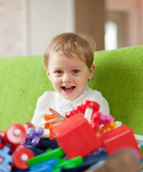Un niño pequeño está sentado en un sofá verde jugando con juguetes.