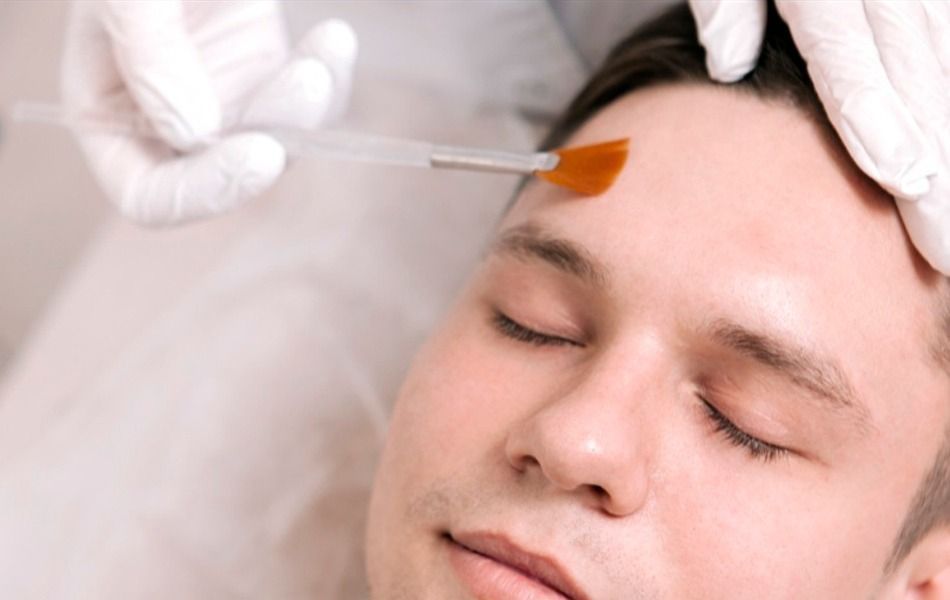 Un hombre está recibiendo un tratamiento facial con un cepillo en la frente.
