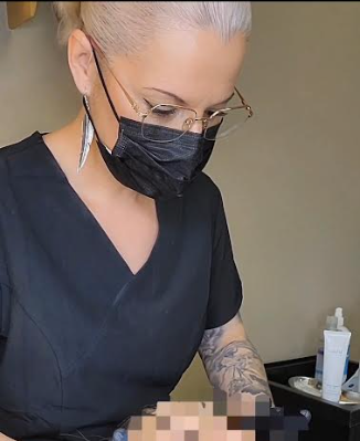 Una mujer con máscara y gafas está trabajando en un tatuaje.