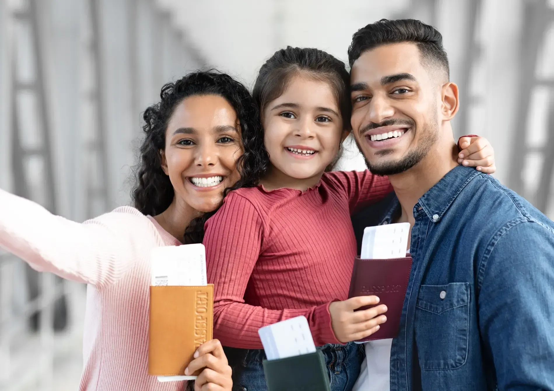 Familia de tres sonriendo, sosteniendo pasaportes y tarjetas de embarque en un aeropuerto.