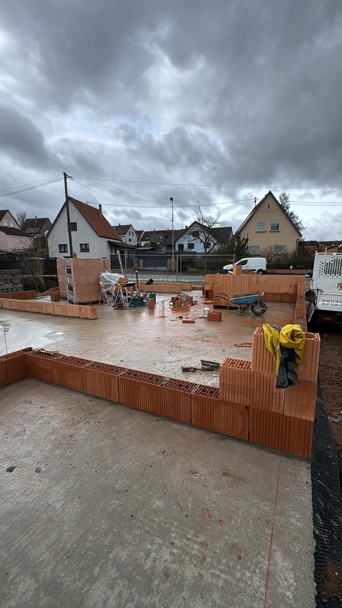 Fondations en briques en construction dans un quartier résidentiel sous un ciel nuageux.