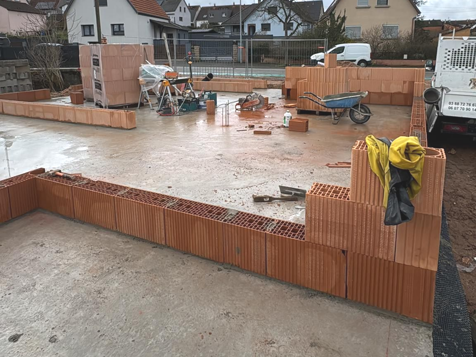 Fondations en béton en construction avec coffrage orange, outils et brouettes sur un chantier résidentiel