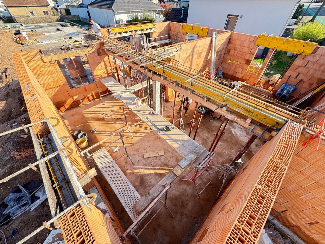 Vue en plongée d'un chantier de construction avec des murs en briques, des échafaudages et des coffrages en béton.