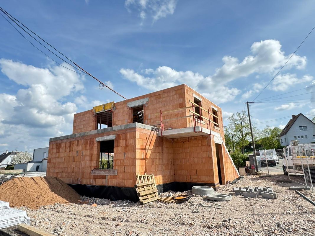 Maison en briques partiellement construite sur un terrain de gravier sous un ciel bleu