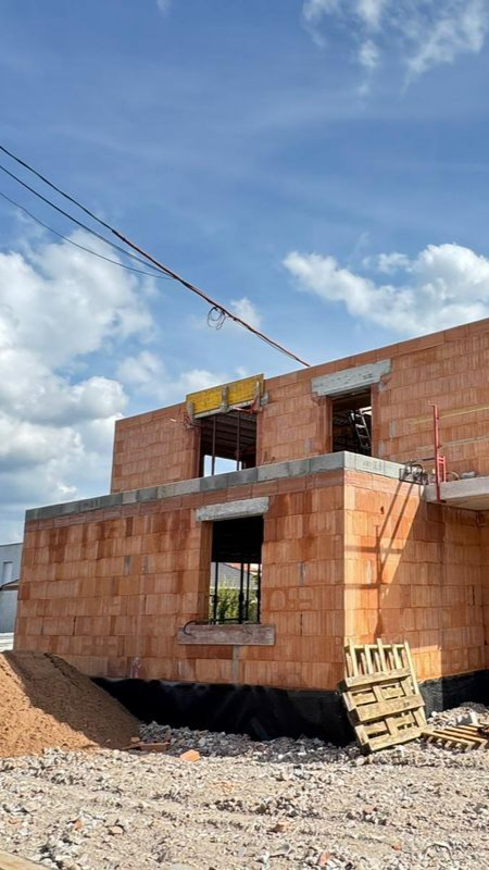 Maison en briques rouges partiellement construite sur un terrain rocailleux sous un ciel bleu