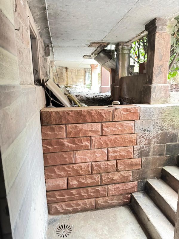 Passage extérieur étroit avec marches, colonnes en béton et mur de briques rouges en construction