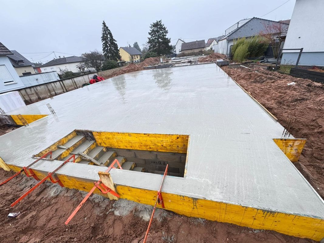 Dalle de fondation en béton en construction avec coffrage jaune et ouvertures pour armatures sur un chantier