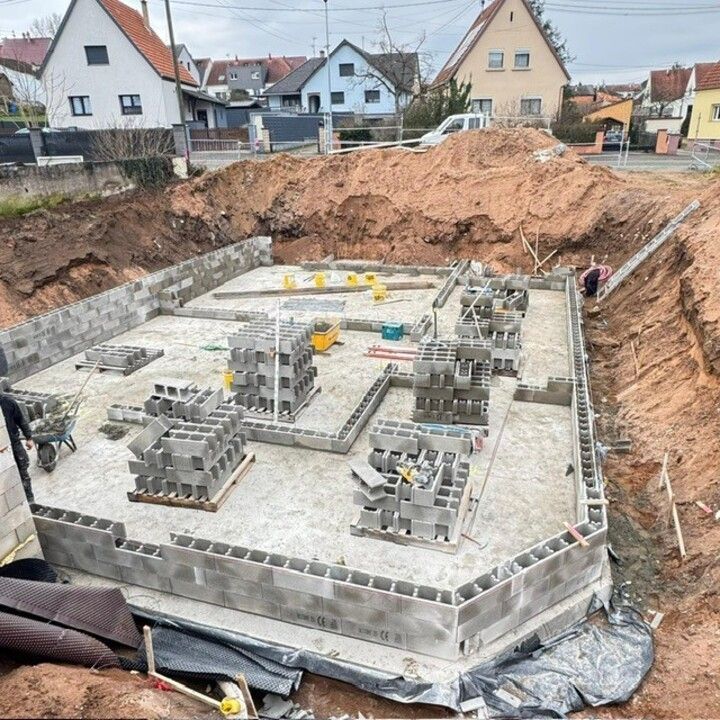 Chantier de construction de fondations avec murs en blocs de béton, armatures et terrassement dans une zone résidentielle
