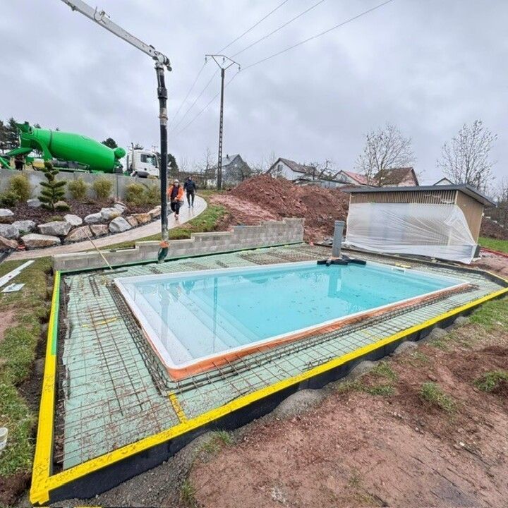 Piscine rectangulaire en construction, avec bordure en béton, marquages jaunes et grue à proximité.