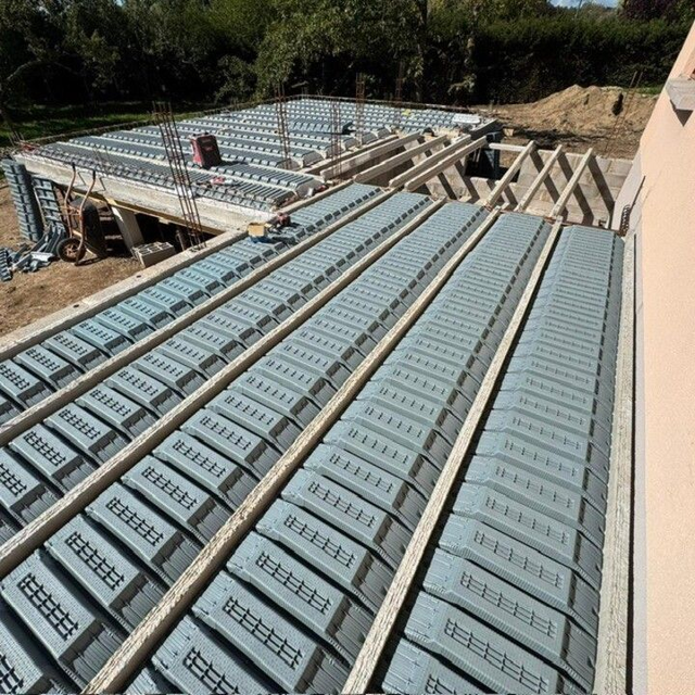 Toiture en construction avec panneaux isolants bleu-gris et charpente en bois apparente sur un site à flanc de colline