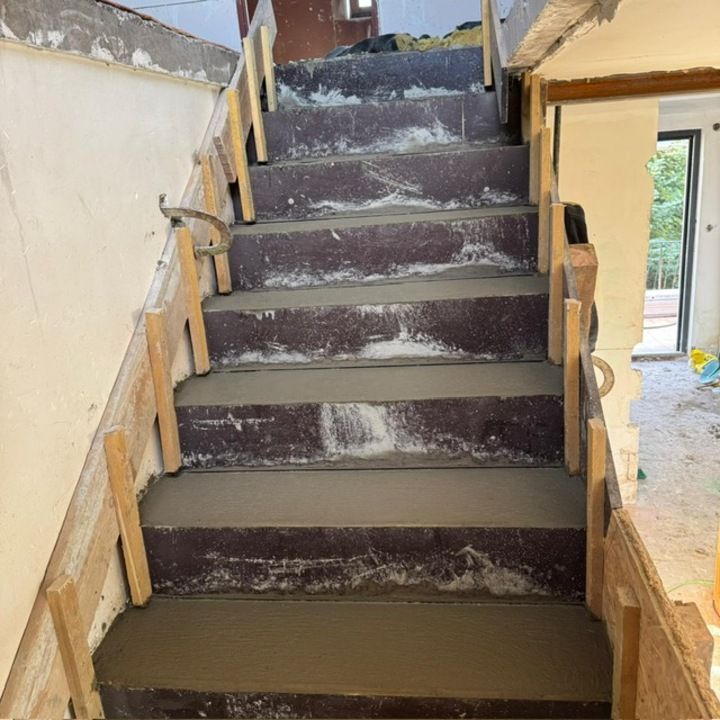 Escalier inachevé avec marches recouvertes de moquette foncée et charpente en bois apparente dans une maison en rénovation