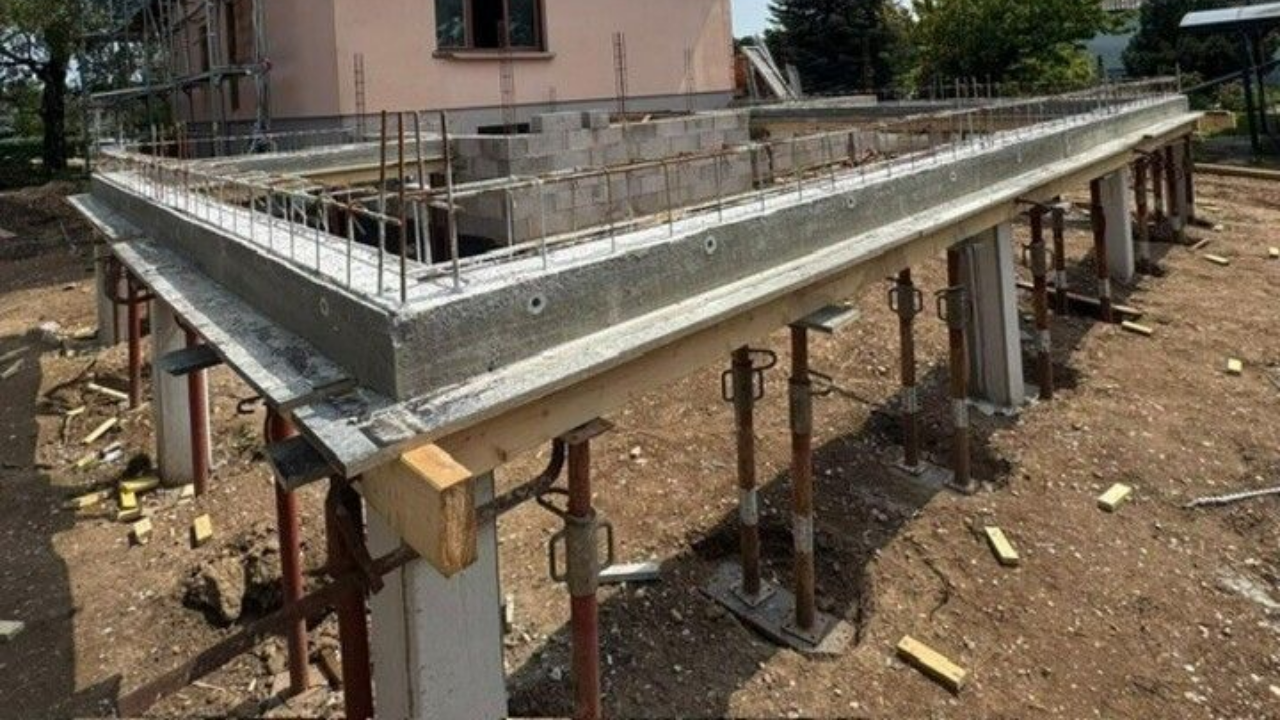 Fondations en béton en construction, avec poteaux de soutien et armatures, sur un terrain en terre.