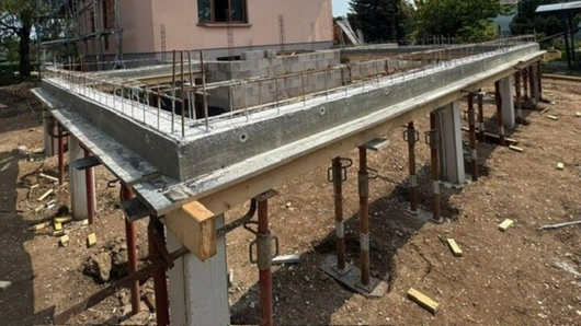 Chantier de construction avec dalle de béton surélevée et colonnes de soutien sur un terrain en terre battue