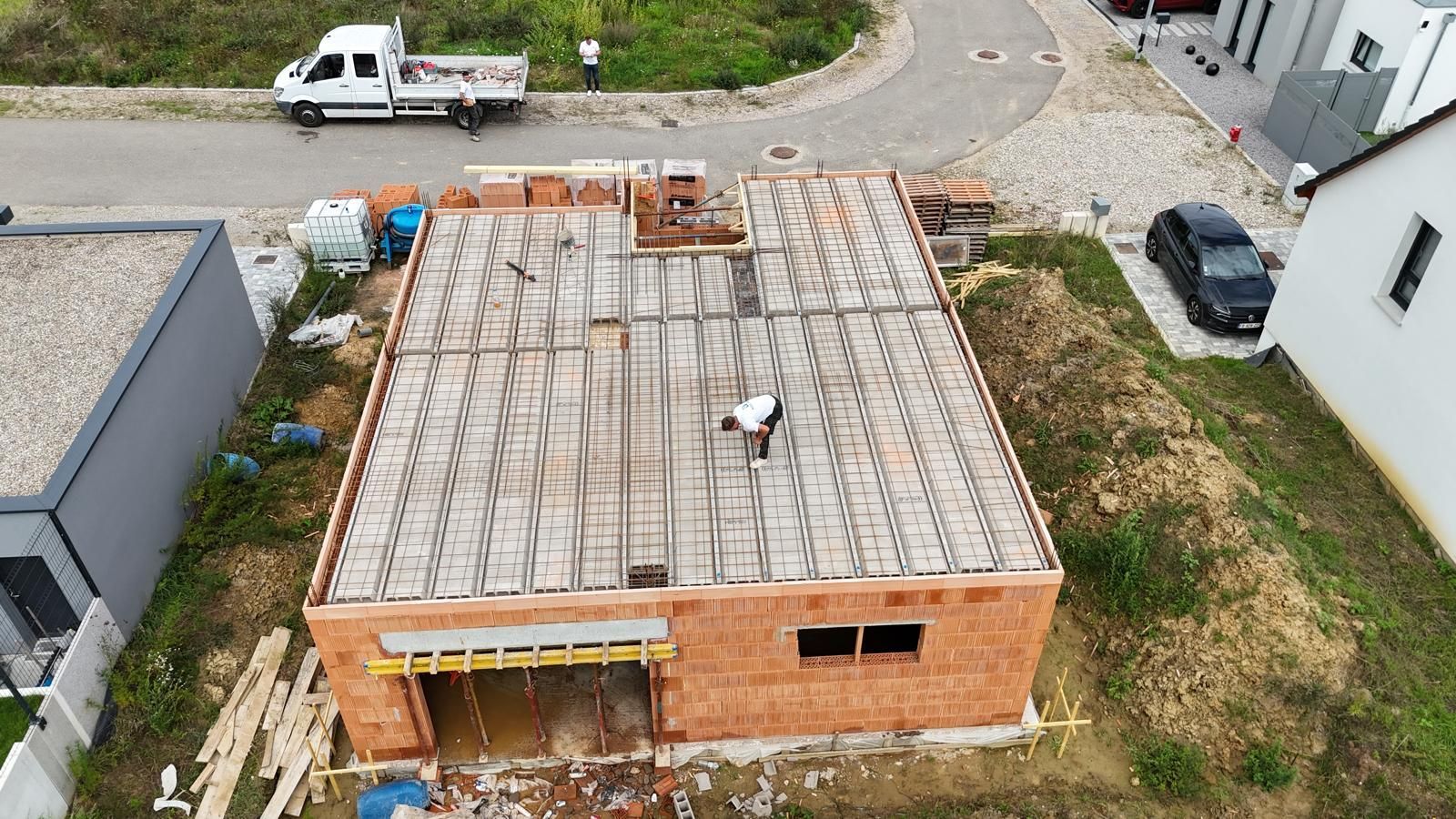 Vue aérienne d'un toit de maison en briques en construction, avec des matériaux éparpillés et une camionnette blanche à proximité.