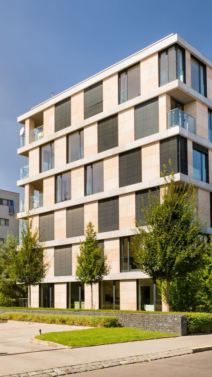 Immeuble d'appartements moderne beige avec balcons, arbres et trottoir gazonné devant