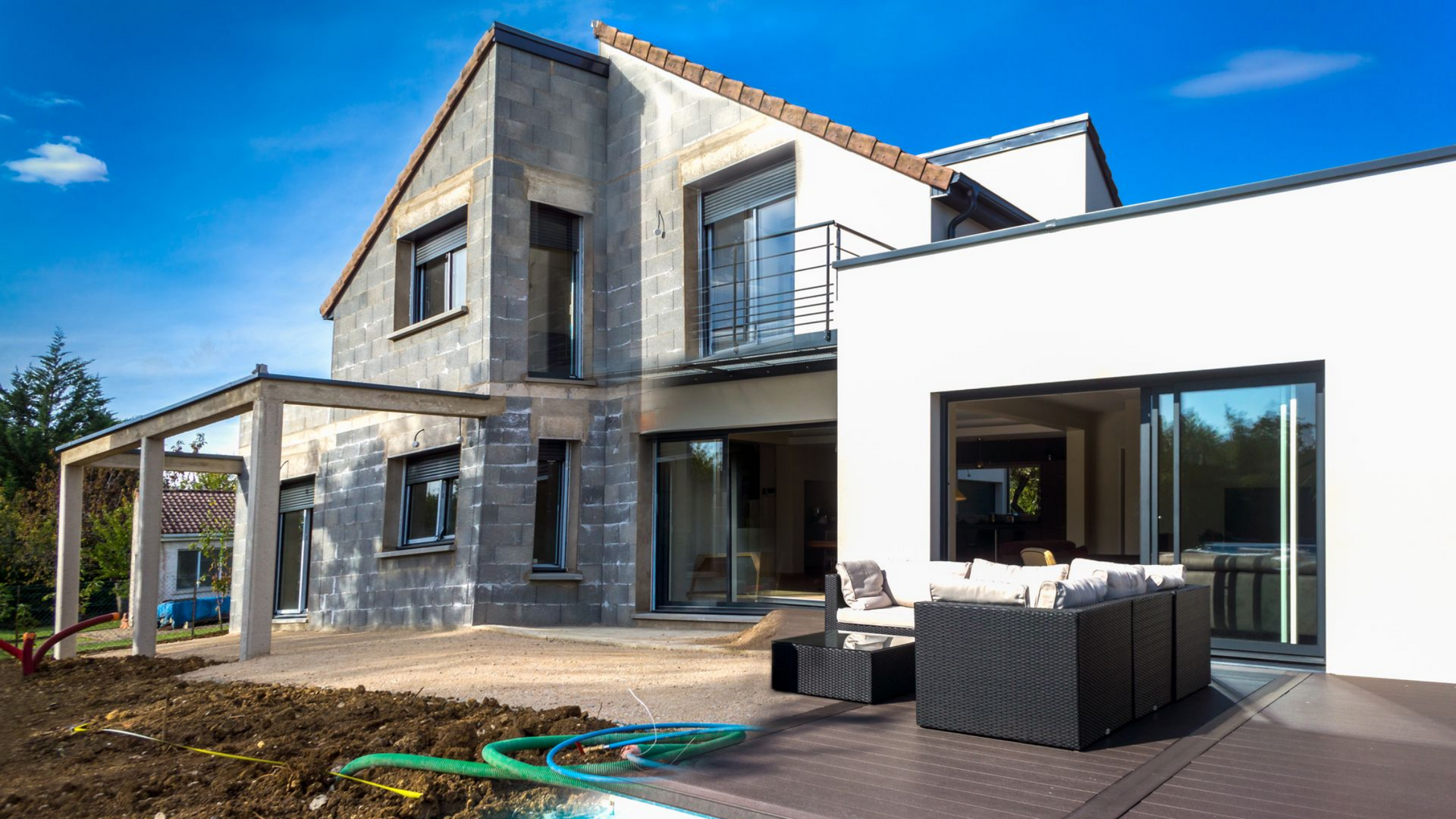 Maison moderne à deux étages avec patio, coin salon extérieur et grandes portes vitrées sous un ciel bleu