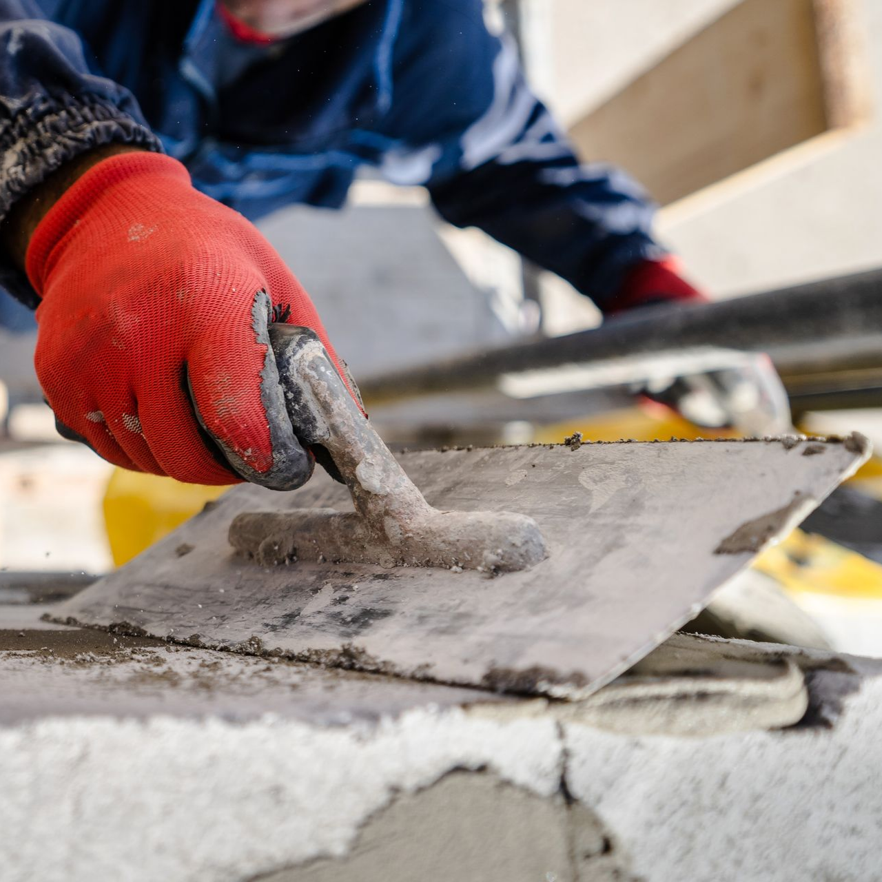 Ouvrier ganté de rouge étalant du béton frais à la truelle sur un chantier de construction
