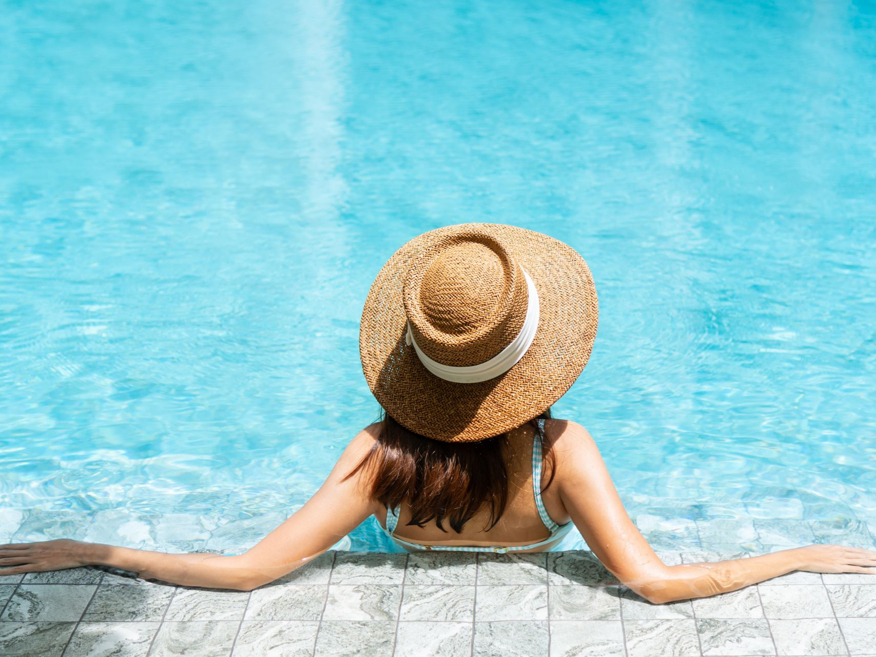 Une personne portant un chapeau de paille se détend au bord d'une piscine d'un bleu éclatant.