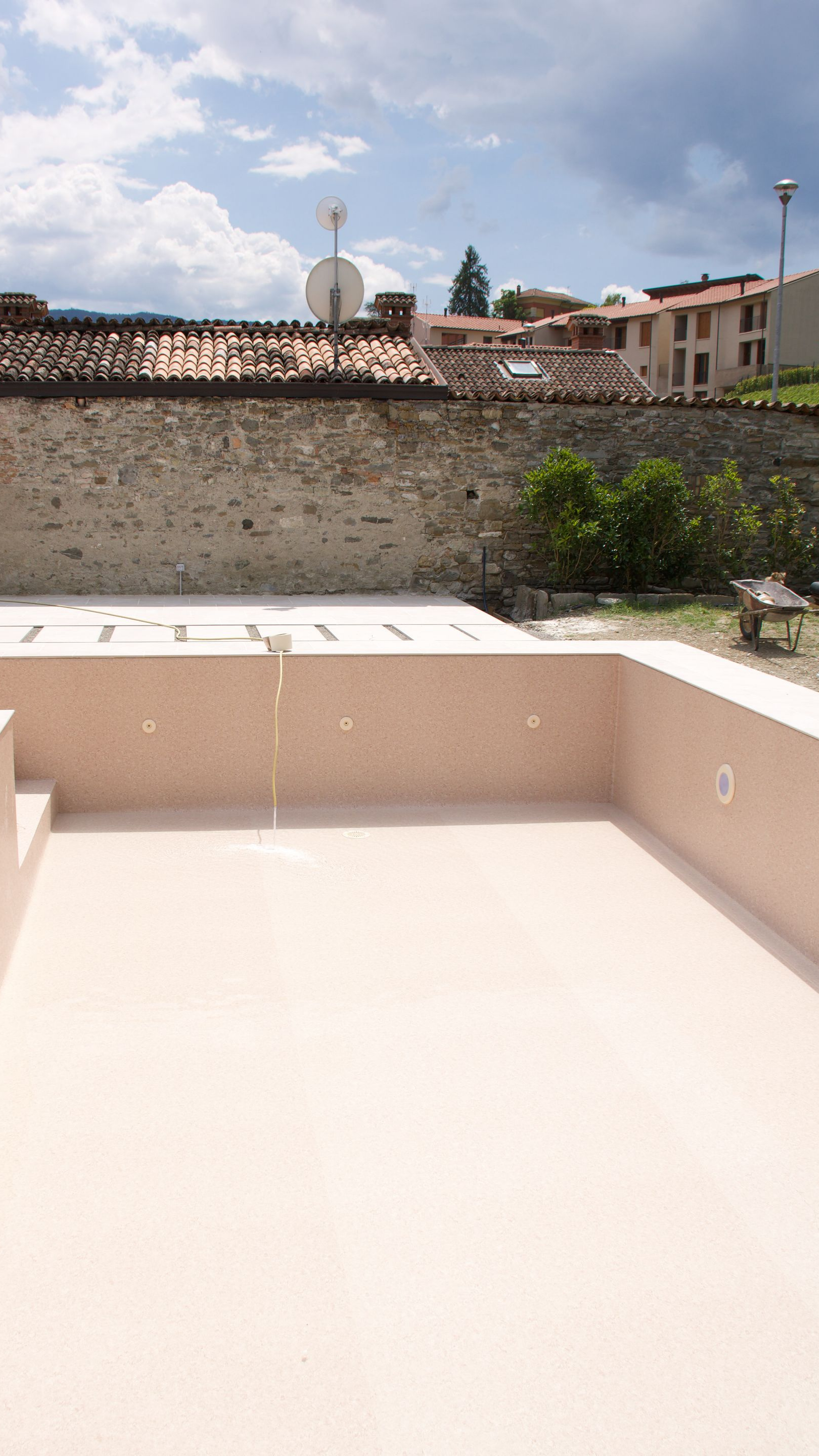 Terrasse sur le toit vide avec une banquette beige intégrée, un mur en pierre et des maisons au loin sous un ciel partiellement nuageux