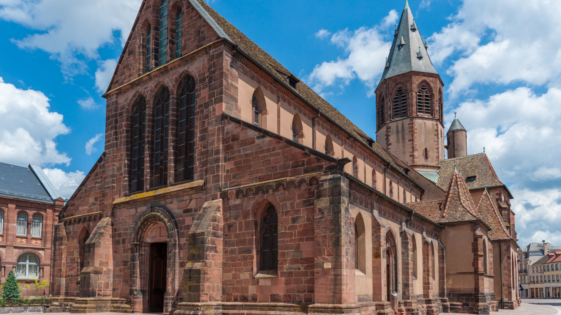 Église historique en briques rouges avec une haute tour et des fenêtres cintrées sous un ciel bleu