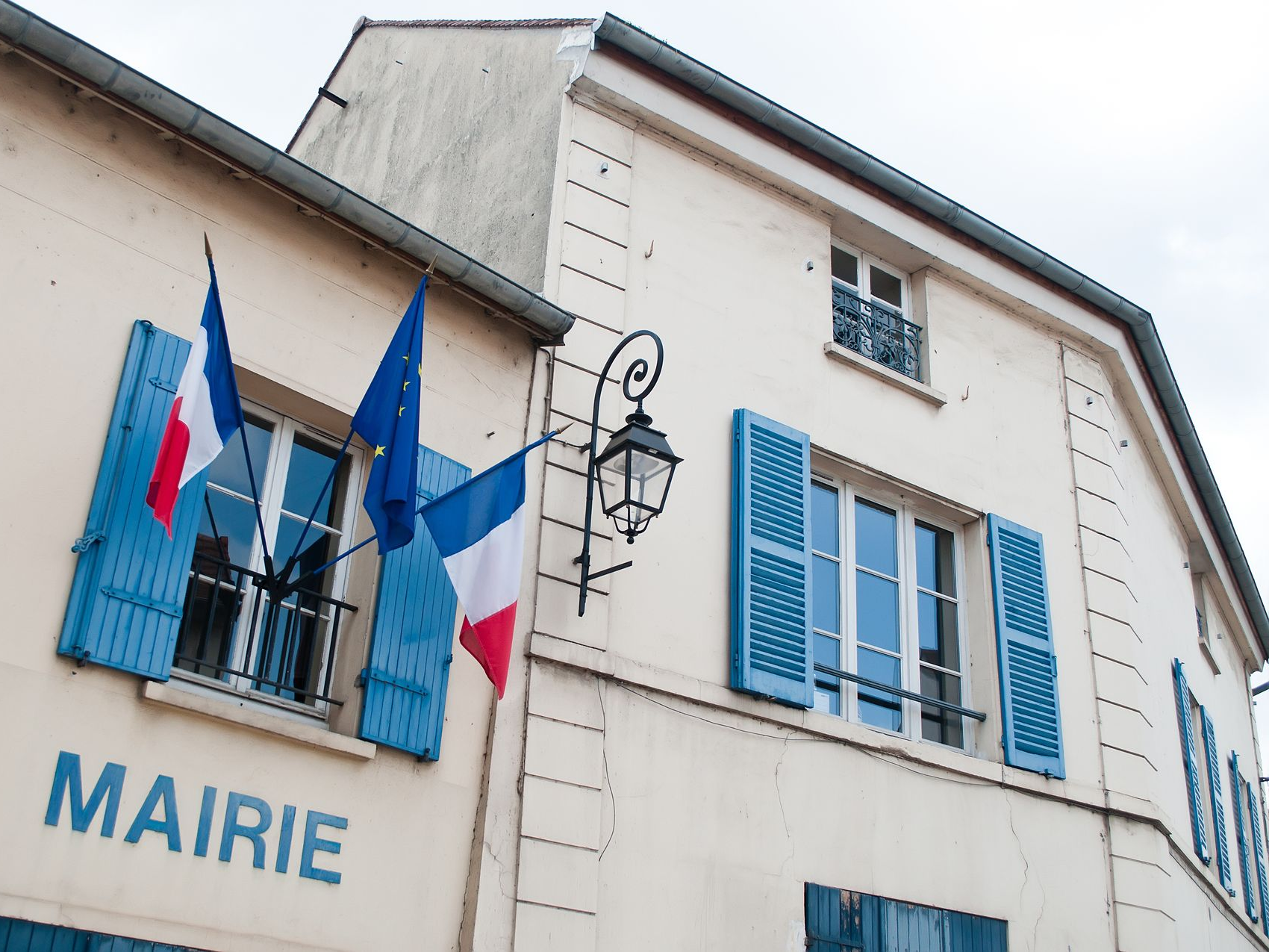 Hôtel de ville français avec volets bleus et drapeaux français au-dessus du mot MAIRIE