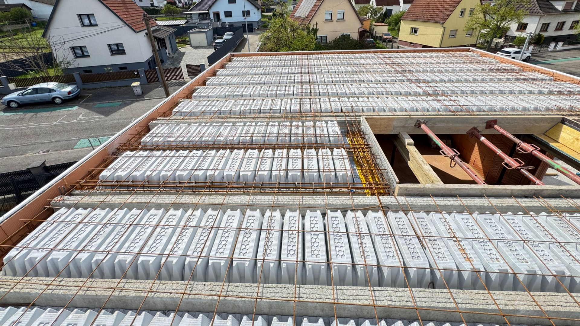 Toiture en construction avec des rangées de panneaux blancs et une charpente en bois apparente dans un quartier résidentiel