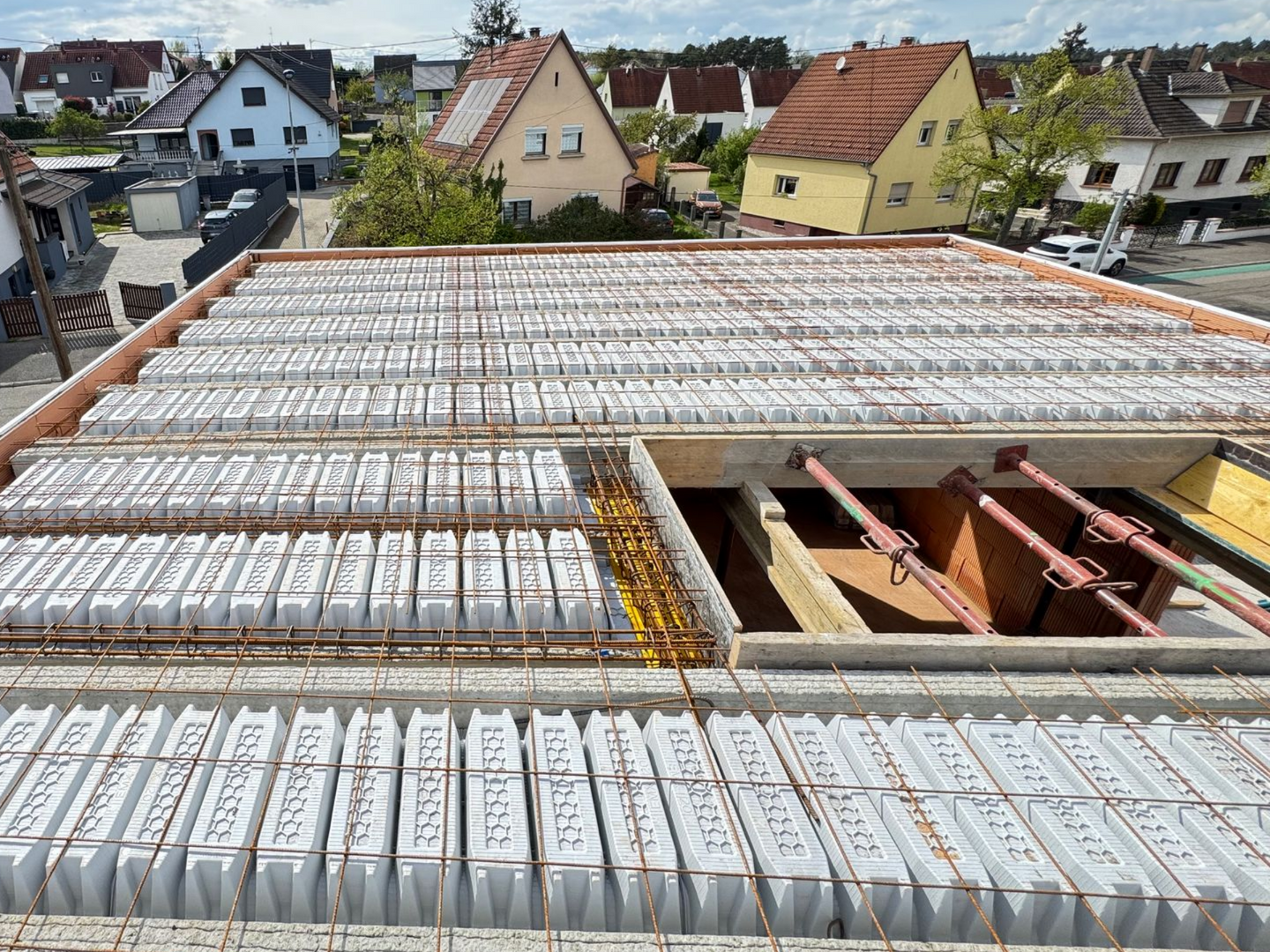 Toiture en construction avec panneaux de toiture blancs, charpente apparente et maisons visibles en arrière-plan