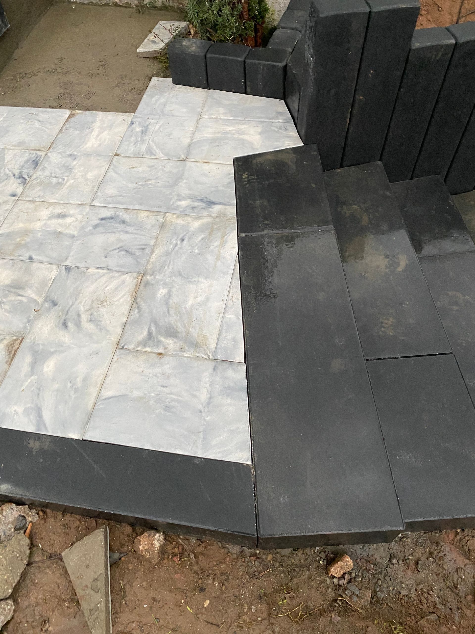 Allée partiellement pavée de dalles de pierre grise et de pavés rectangulaires foncés en cours de construction