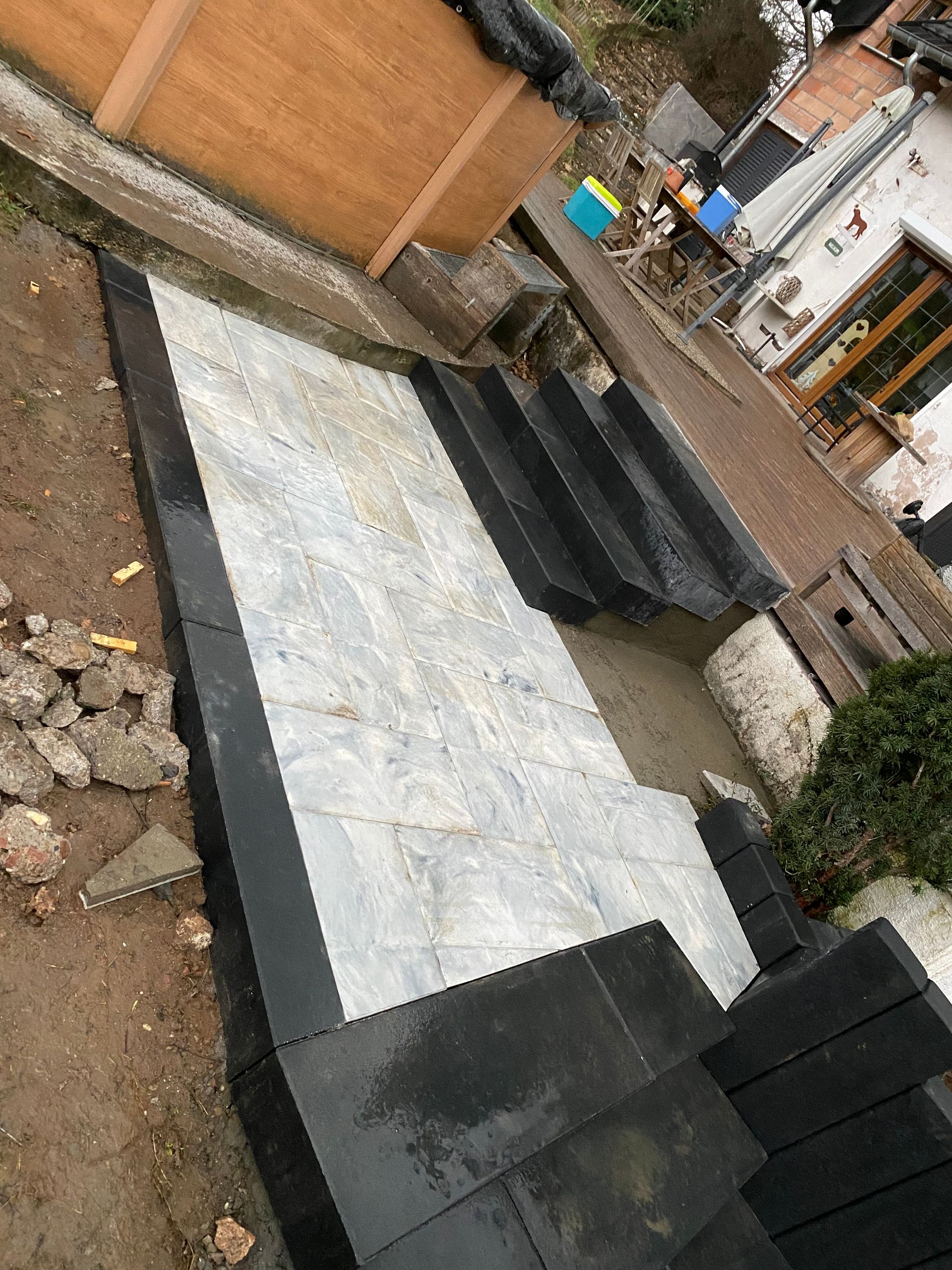 Plateforme extérieure en béton à côté d'un escalier et d'un sol en terre battue, avec des sections noires et blanches dans une cour