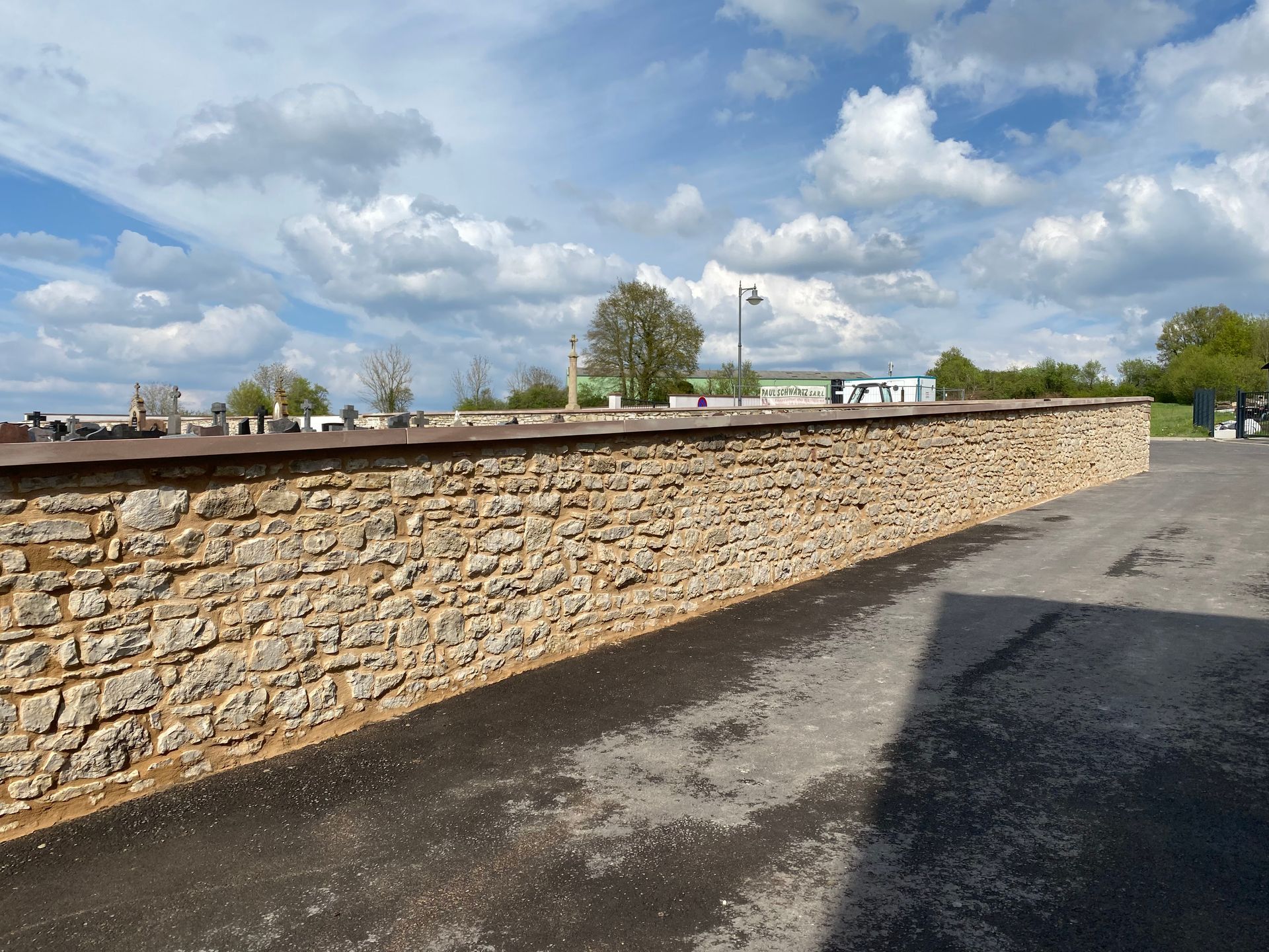 Mur de pierre à côté d'un terrain pavé sous un ciel bleu partiellement nuageux