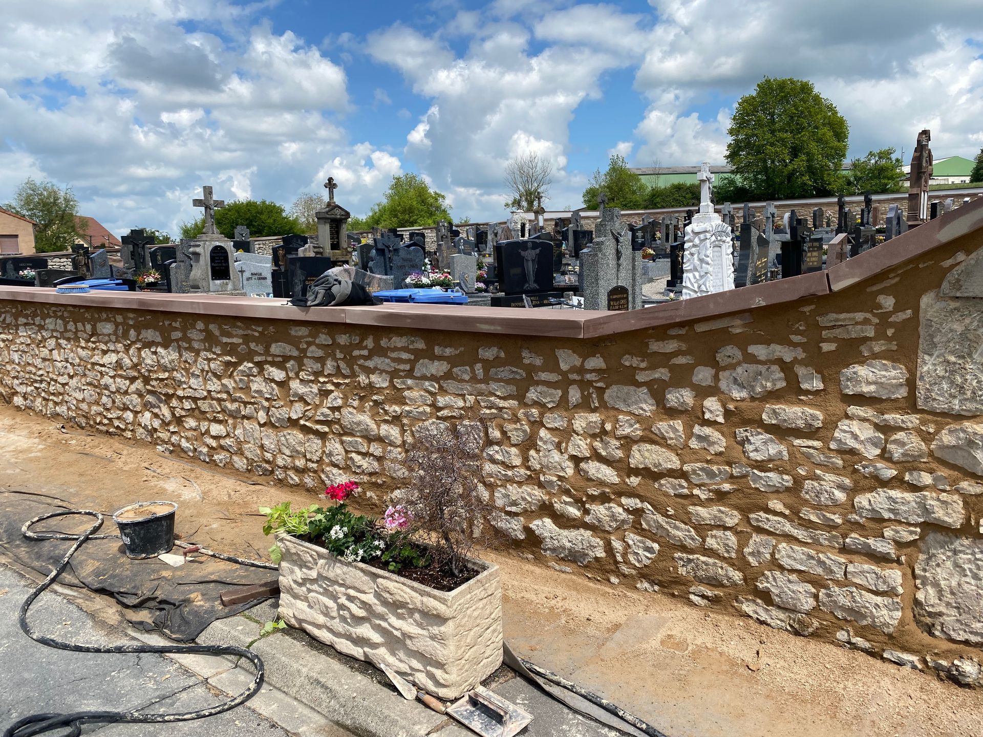 Mur de cimetière en pierre avec des pierres tombales, des fleurs et un ciel nuageux en arrière-plan