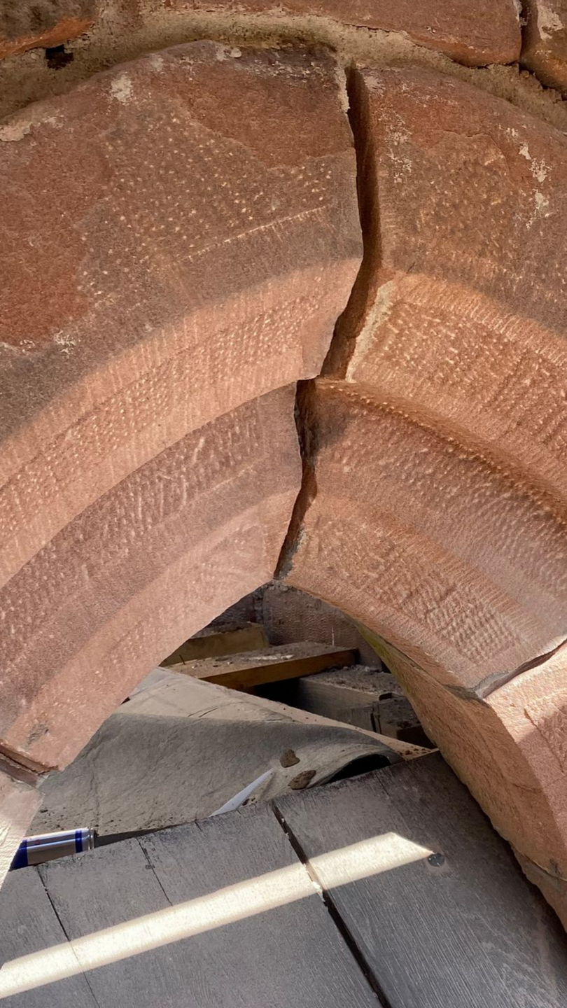 Gros plan sur une arche en briques de terre cuite fissurée, avec un support en bois en dessous.