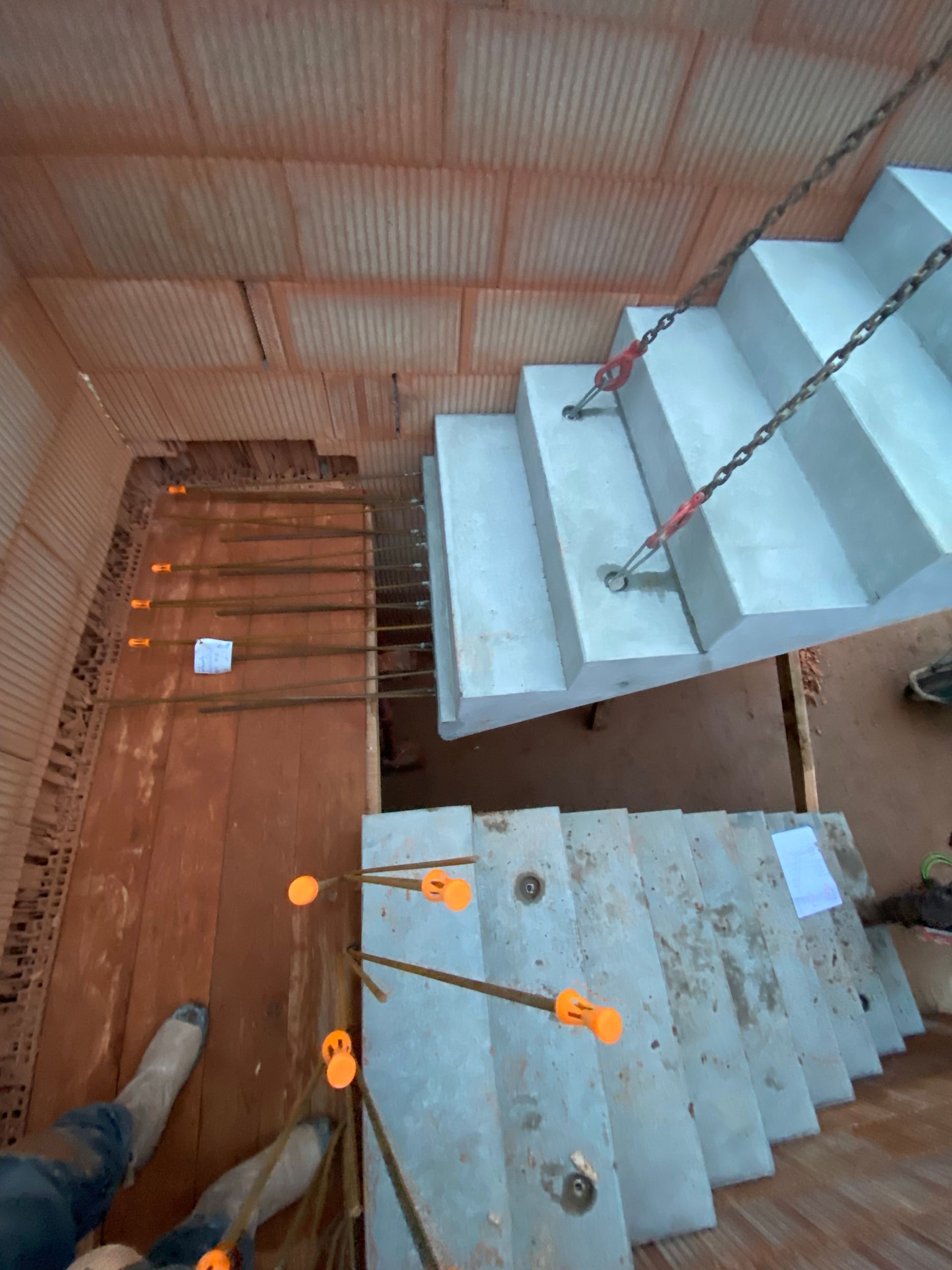 Escalier intérieur avec marches en béton blanc, rampes orange et mur en tôle ondulée en dessous.