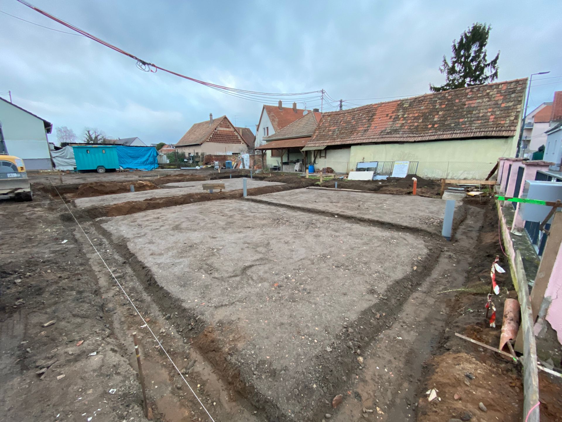 Terrain nu avec fondations en béton à côté de maisons, avec coffrage en bois et ciel nuageux